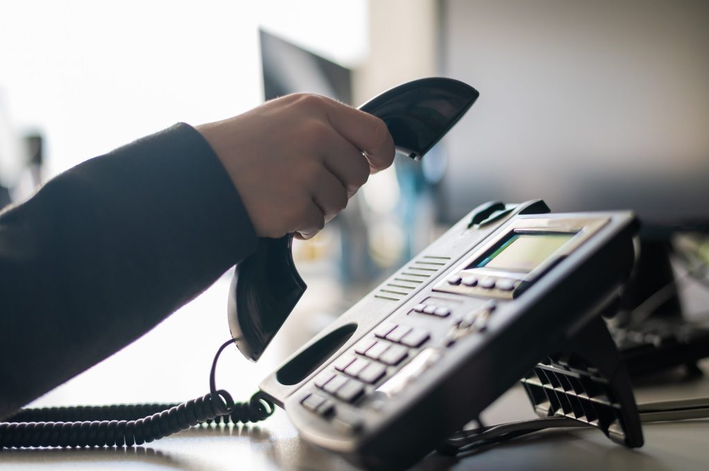 Close-up of the hand of a female office worker dialing a number on a landline phone. Faceless woman secretary calls on the phone