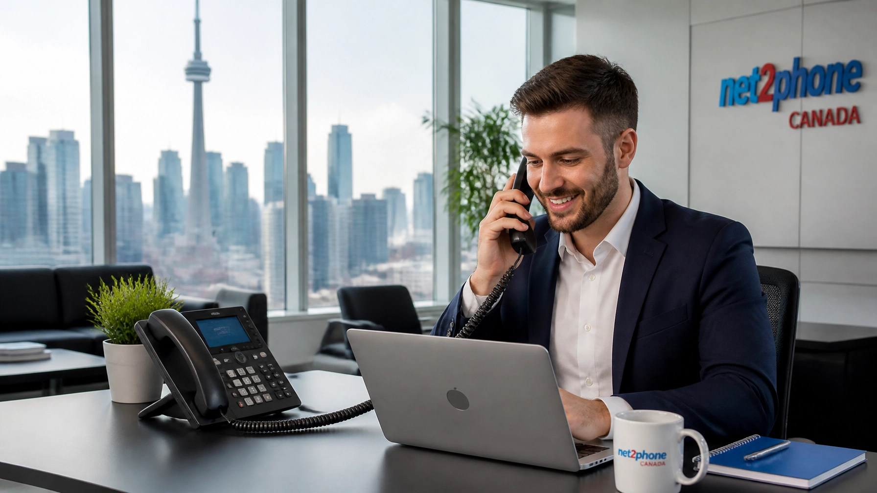 YHF_vfgec3_ - Voiswitch - Voiswitch Businessman at a desk talking on a corded office phone while working on a laptop, with a net2phone Canada sign in the background.